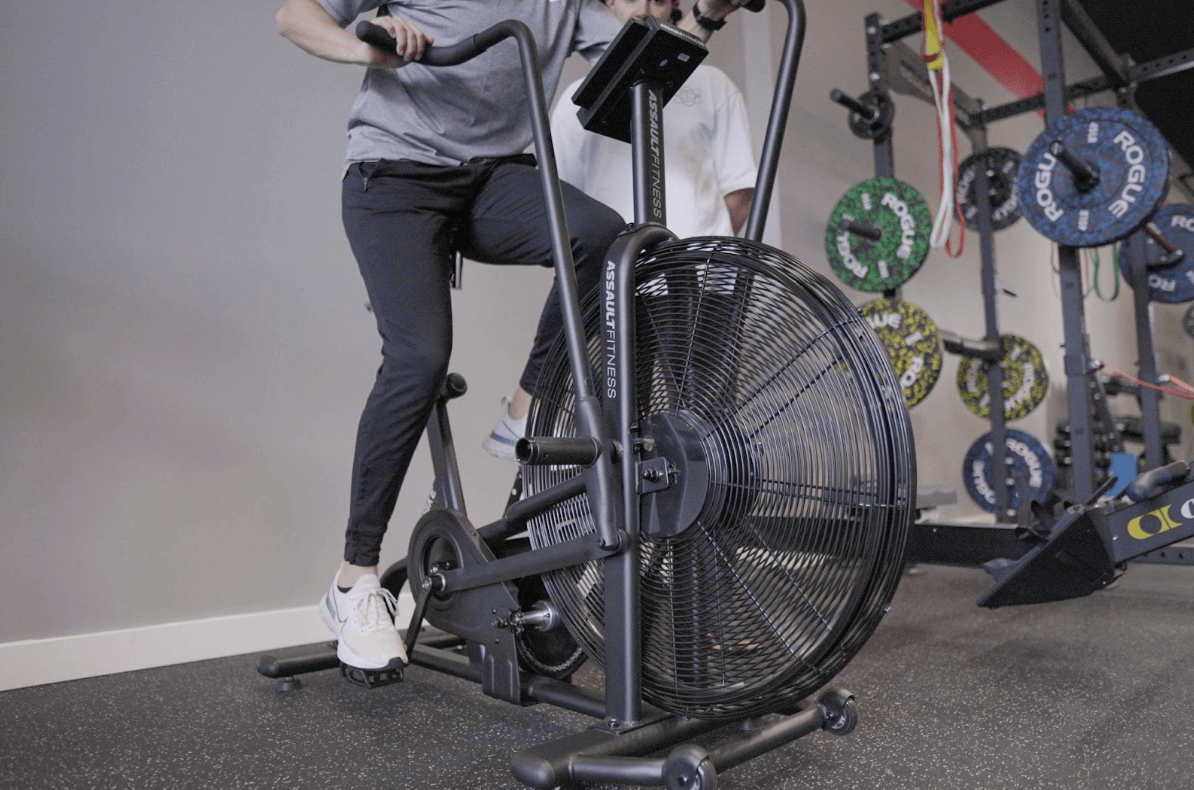 Client effectuant un entraînement sur airbike avec son entraîneur personnel à Montréal chez Studio Fit U, mettant en avant notre méthode holistique personnalisée, offrant un support nutritionnel et une évaluation orthopédique complète, dans notre gym privé à Montréal.